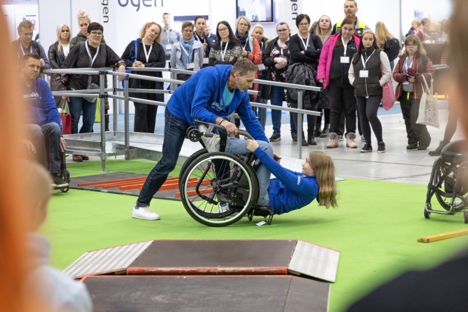 Apuvälineradalla opastetaan avustamaan pyörätuolikäyttäjää oikein ja turvallisesti. Kuvassa yleisö seuraa esitystä radalla.