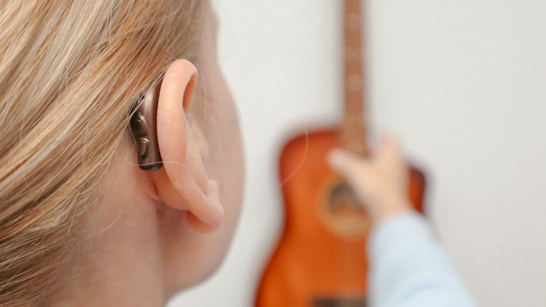 A woman with hearing loss can hear and play guitar again using a hearing aid. Adult woman with hearing aid behind the ear can hear sounds.