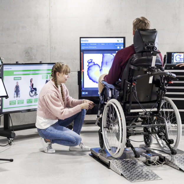 Metropolian Fitting station: henkilö pyörätuolilla mittauspisteellä, edessä pari isoa näyttöä, jotka kertovat tietoa istmisesta.