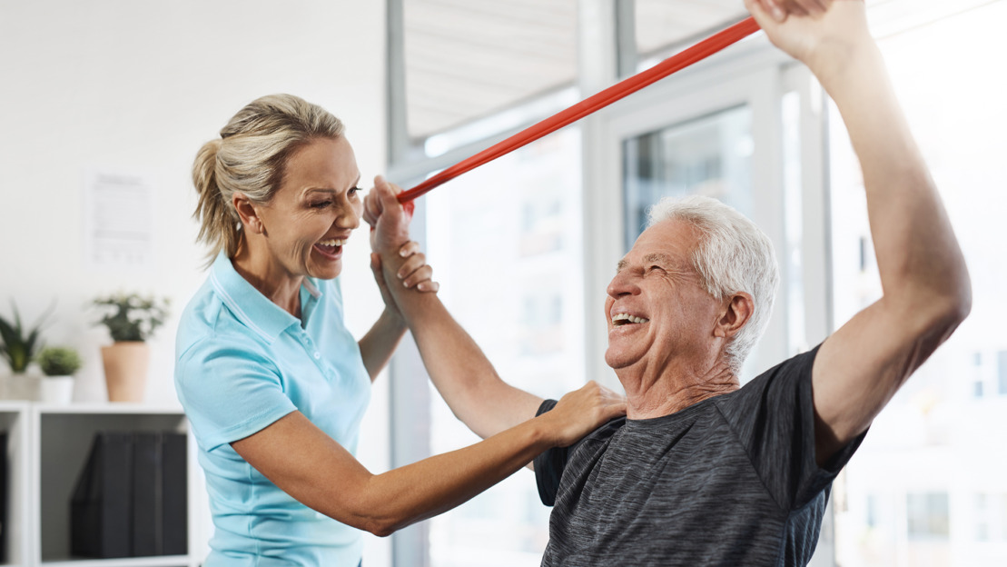 Physical therapy, stretching band and senior patient with medical support, help and happy for healthcare services. People, doctor or chiropractor consulting with elderly client for shoulder strength.