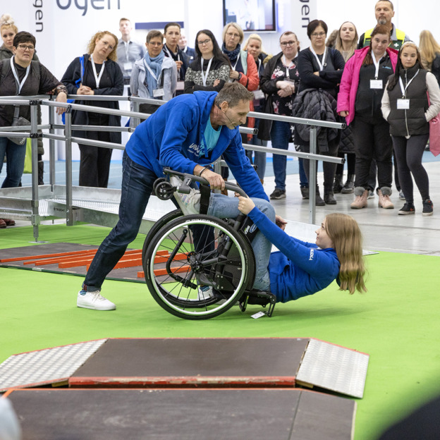 Apuvälineradalla menossa opastus, kuinka avustetaan pyörätuolilla kaatunut henkilö ylös.